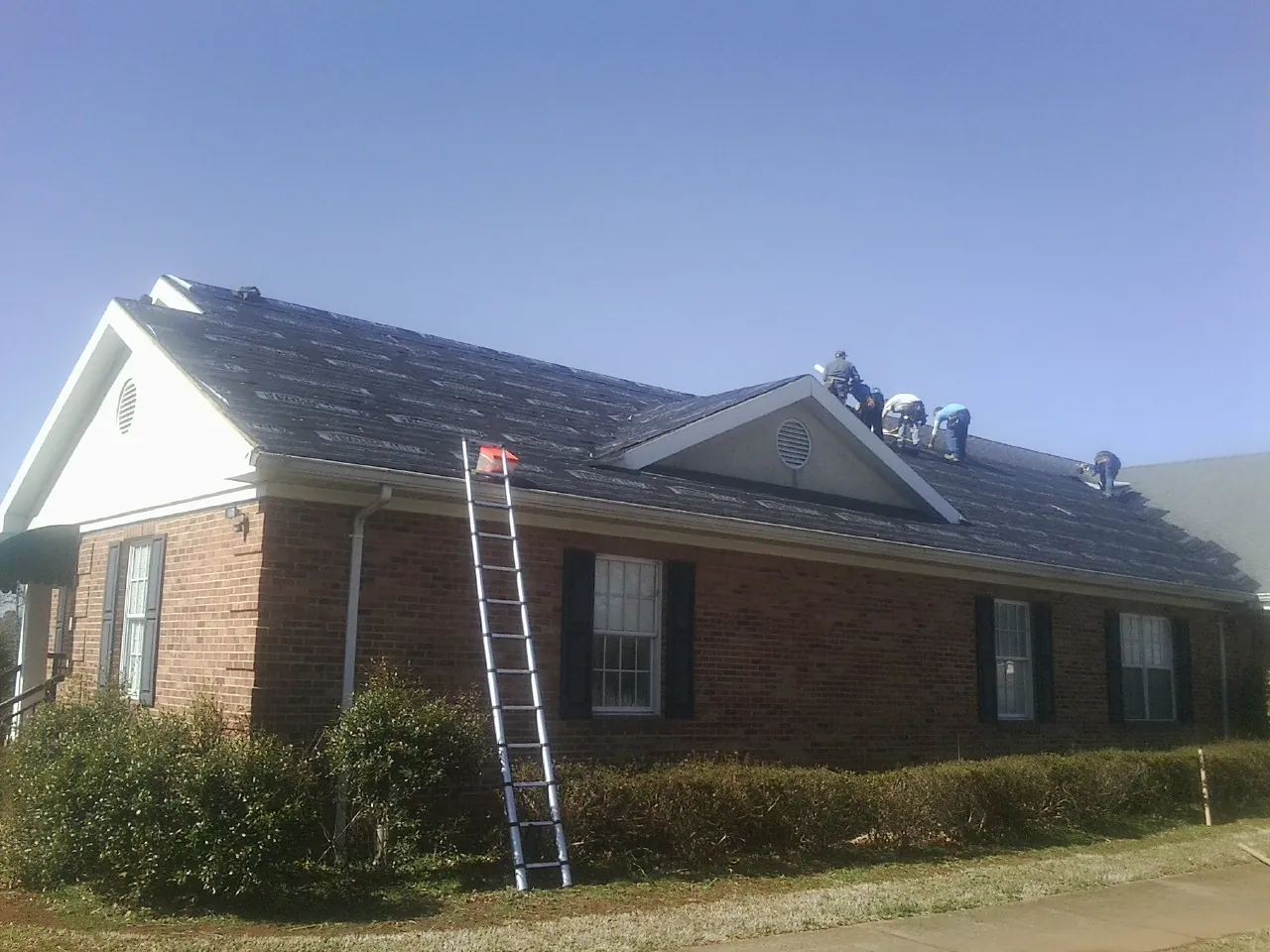 Crew tearing shingles off a brick ranch roof with a ladder set — Metal Roof Repair work by our crew in Banning
