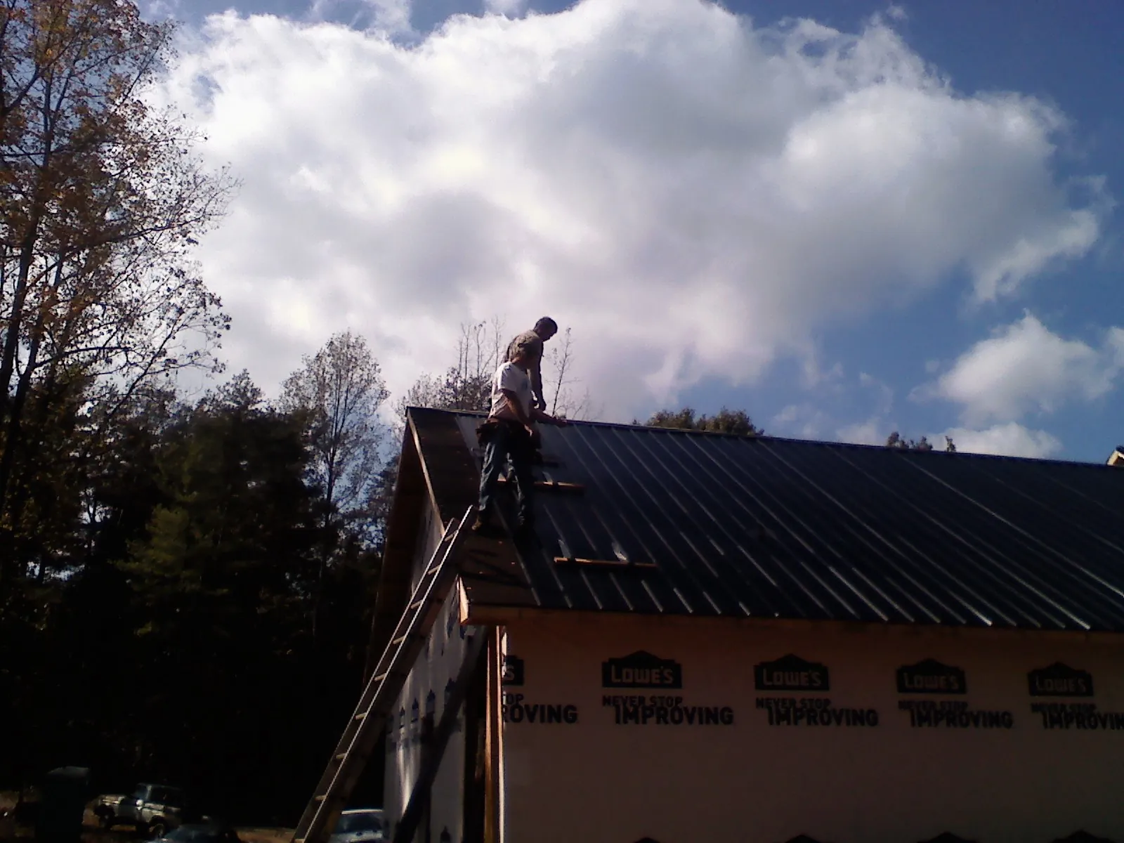 Roofer fastening dark metal panels high against a cloudy sky, from a Roof Inspection job in Banning
